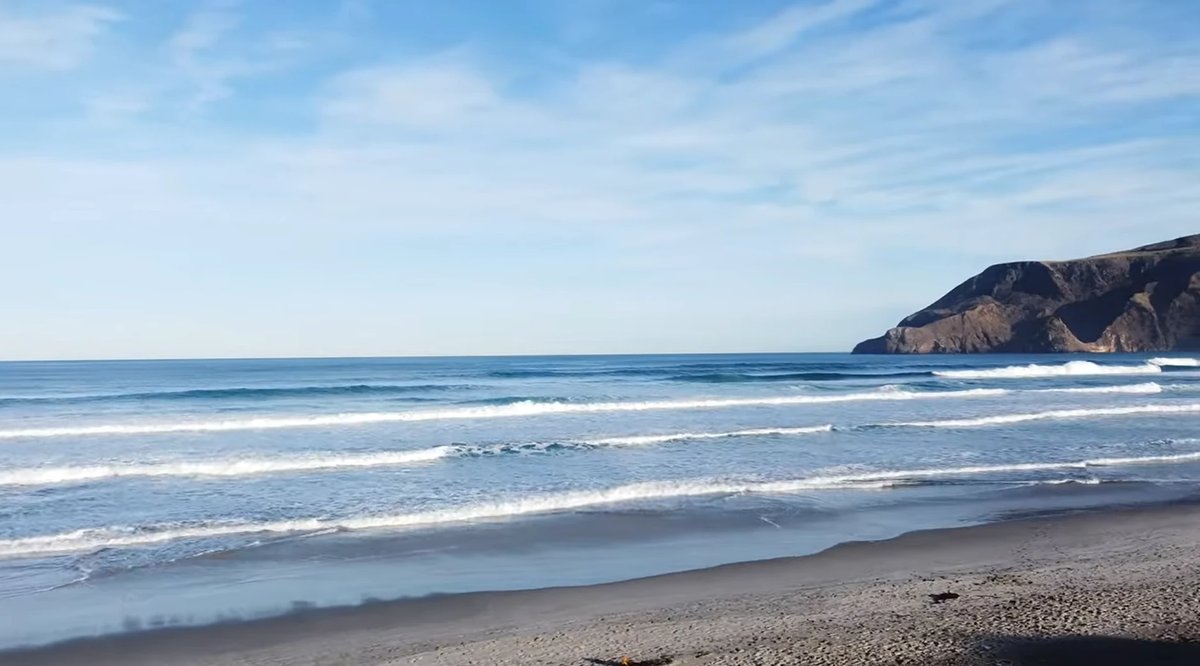 Lines of swell wrap toward the rocky point on a bright, offshore afternoon, Allans Beach surf spot, Dunedin / Otago, New Zeal