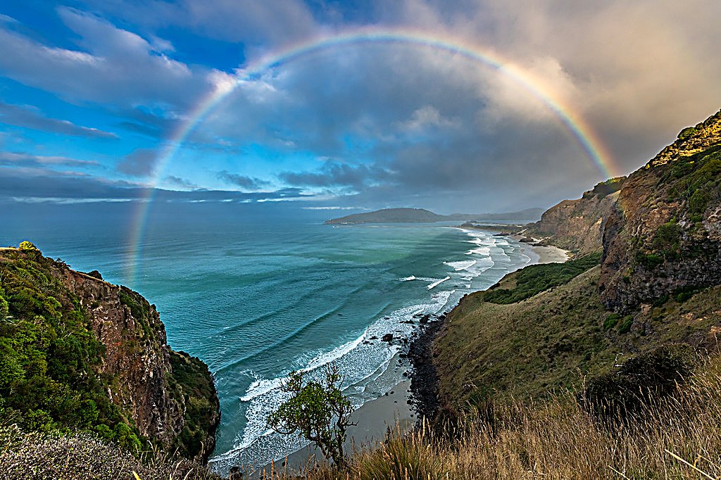 A full rainbow arches over the Otago coast after a passing shower, the wild backdrop to a southern surf, Aramoana surf spot, 