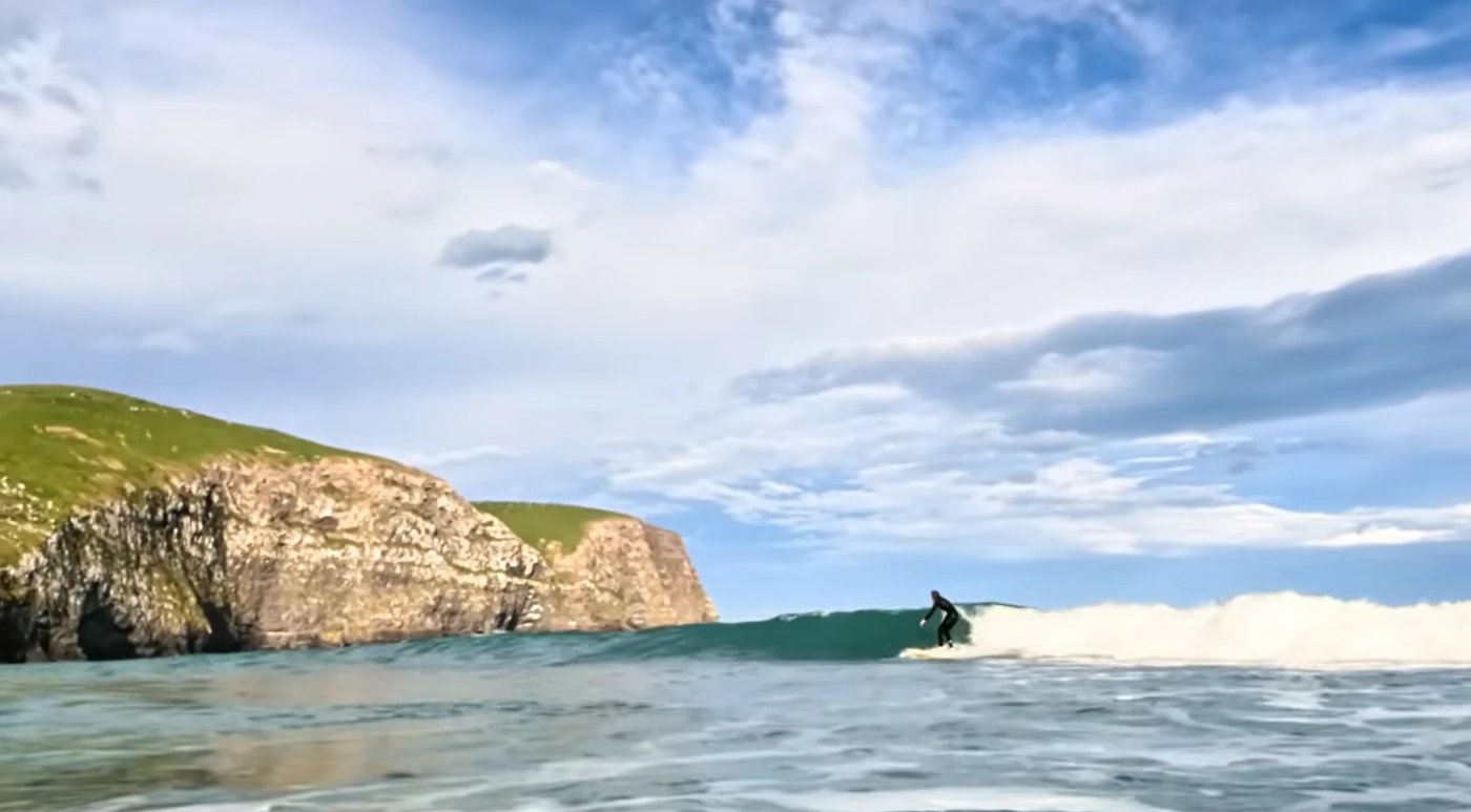 A surfer slides along an open wall below the towering headland cliffs that wrap around Hickory Bay, Hickory Bay surf spot, Ca