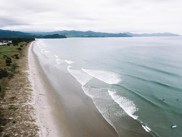 Aerial of the long beach with lines rolling in on a working day, Matarangi surf spot, Coromandel, New Zealand.