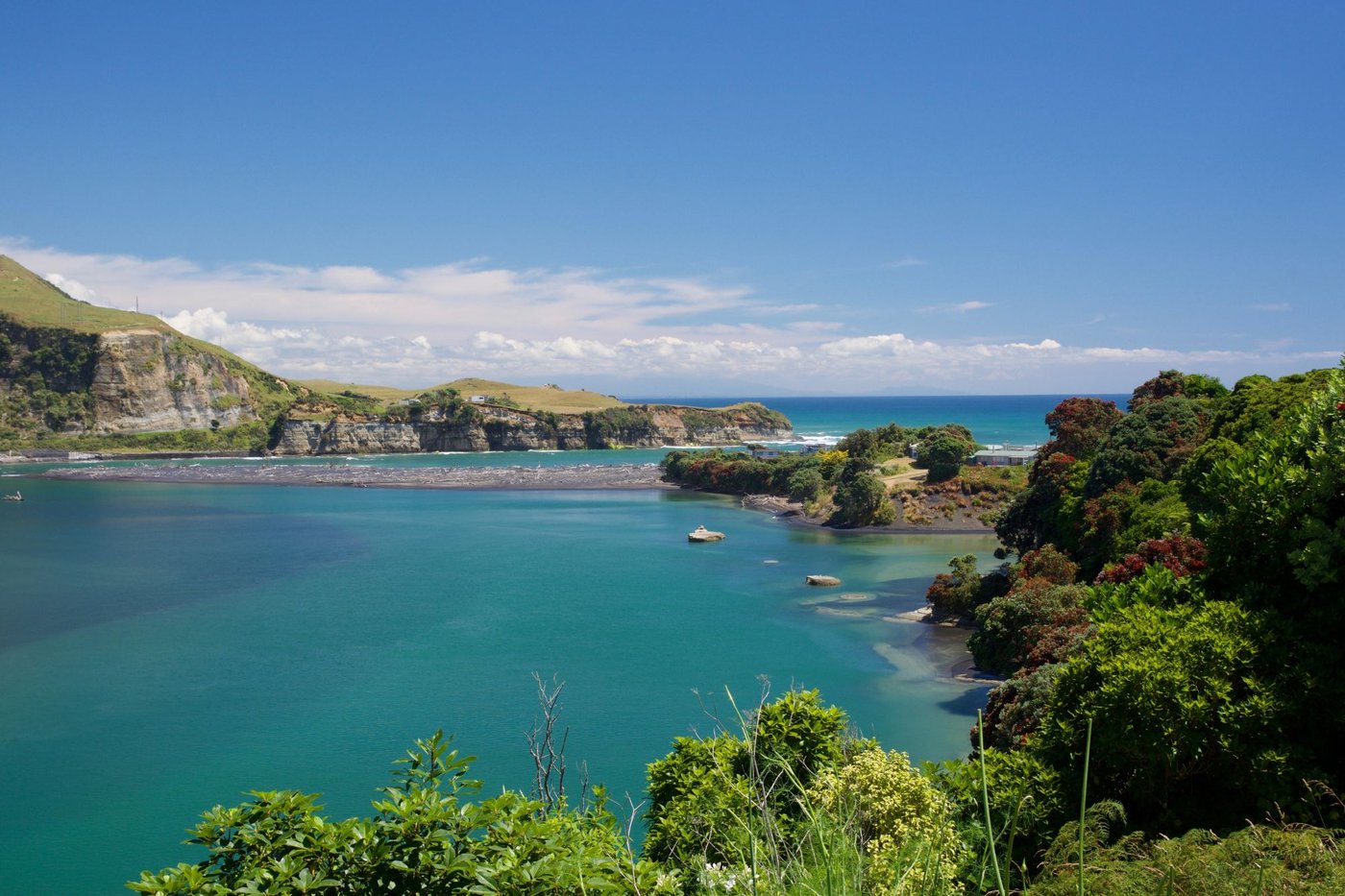 Summer light over the Mōkau river mouth, pōhutukawa in bloom along the banks and open sea beyond the bar, Mōkau surf spot, Ta