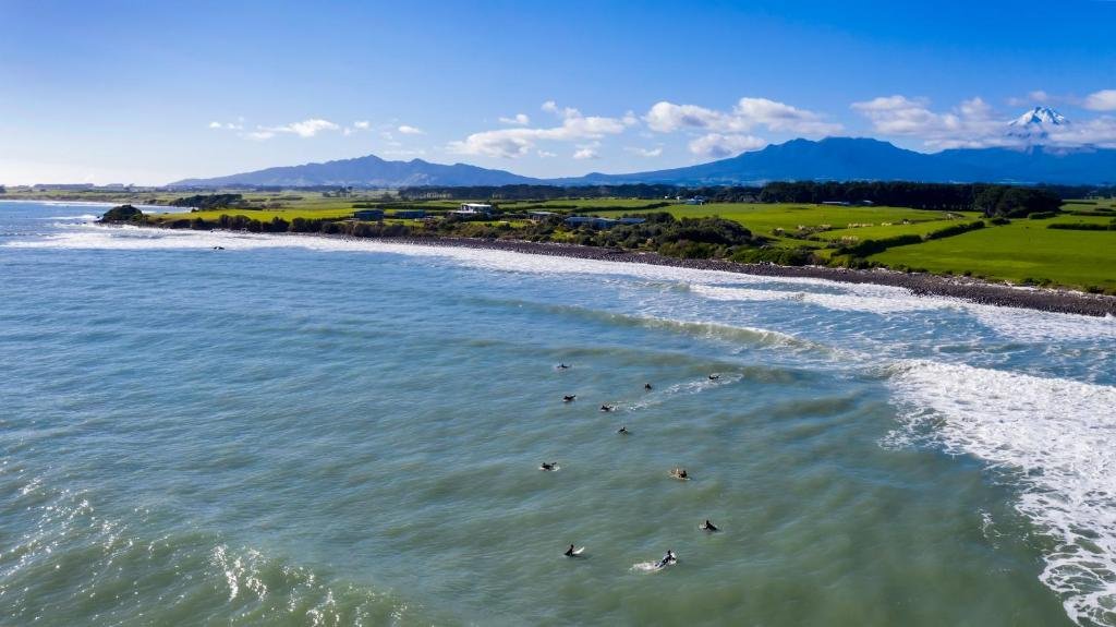 A relaxed lineup waits on the next set, Mt Taranaki standing over the ring plain paddocks behind the break, Ōkato surf spot, 