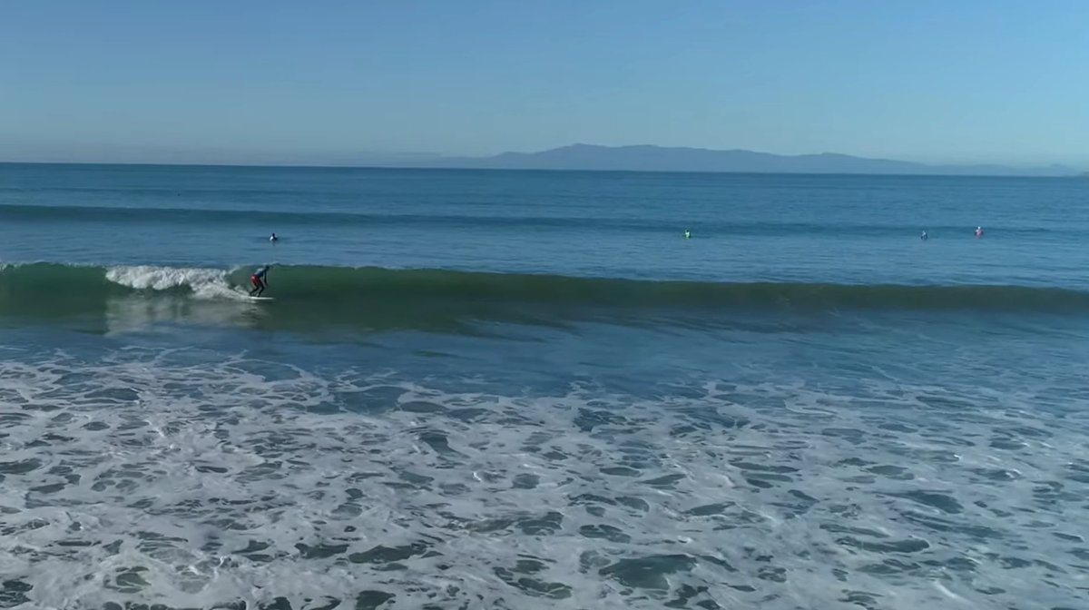 A surfer slides a glassy one with the deep-south ranges hazy on the horizon, Ōraka / Colac Bay surf spot, Catlins / Southland