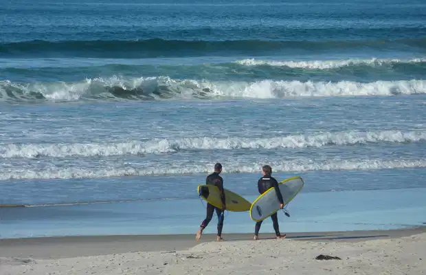 Two surfers walking to the beach for a shoulder-season session, Pāpāmoa surf spot, Bay of Plenty, New Zealand.