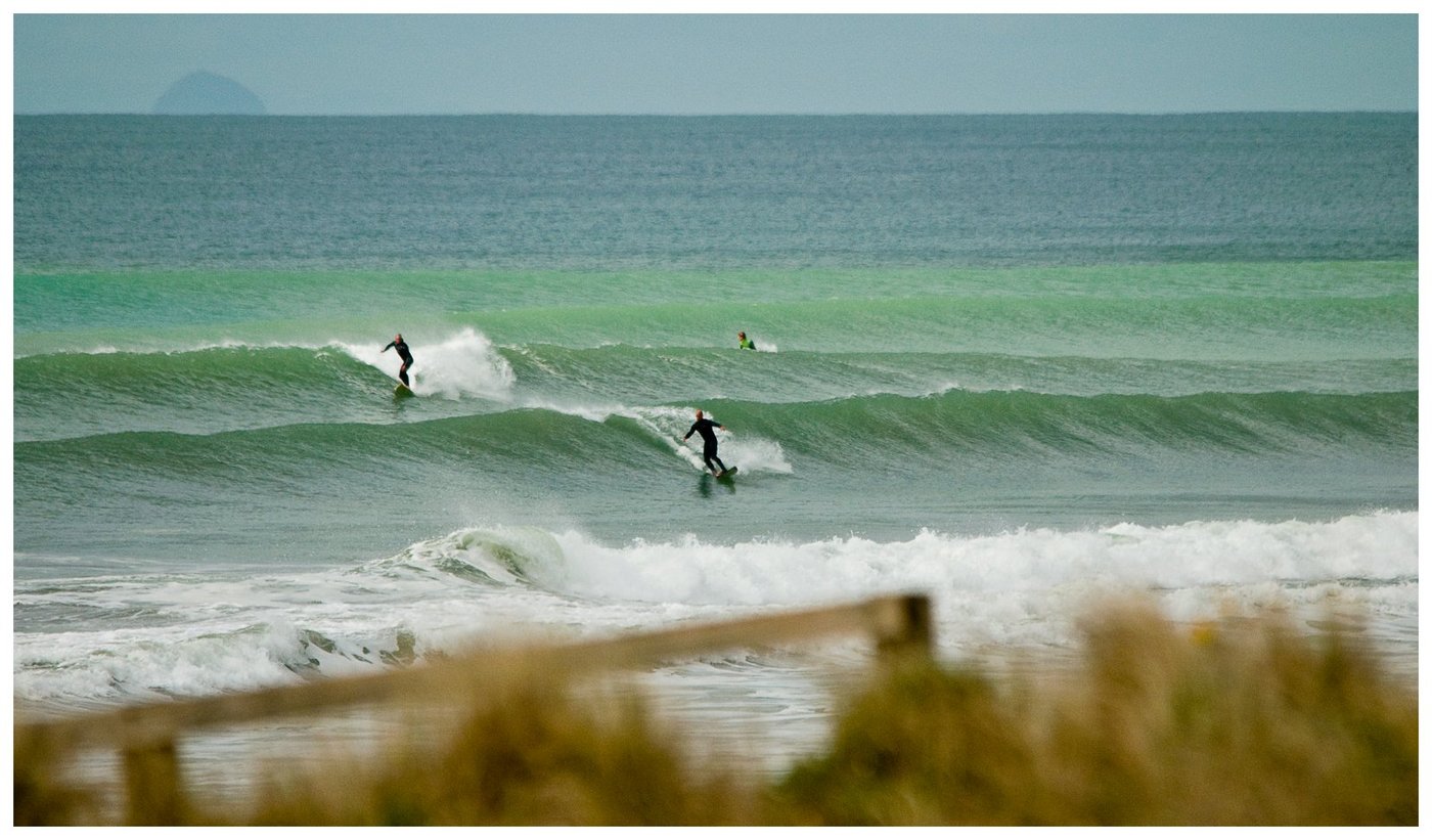 Two surfers on a clean wave with Mōtītī Island in the distance, Pāpāmoa surf spot, Bay of Plenty, New Zealand.