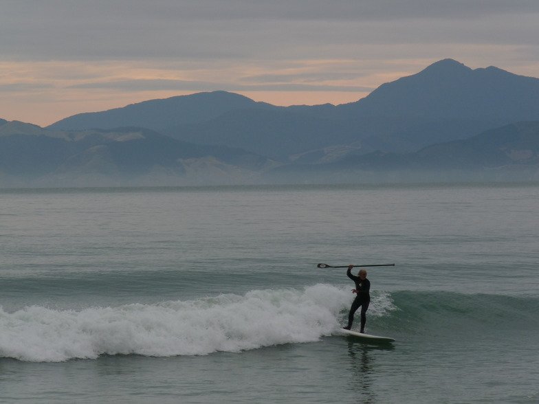 A paddler glides across a soft dusk peeler, the ranges hazing into pastel light across Tasman Bay, Ruby Bay surf spot, Marlbo