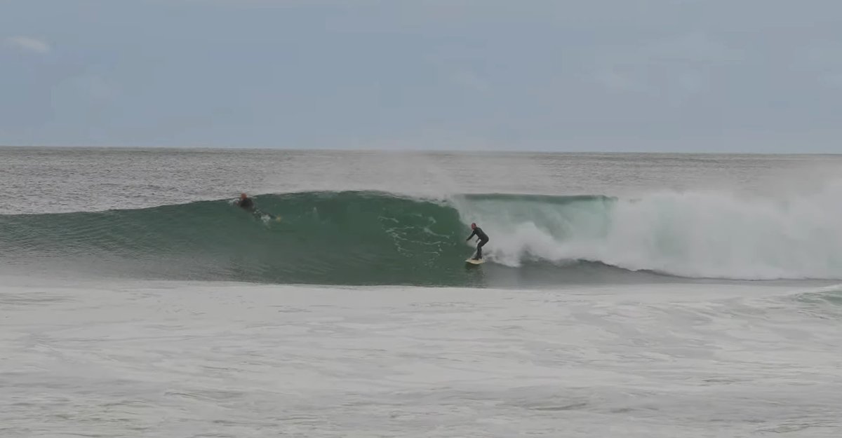 A meaty green A-frame swings through, one surfer up and riding while another scratches over the top, Schnappers Point surf sp