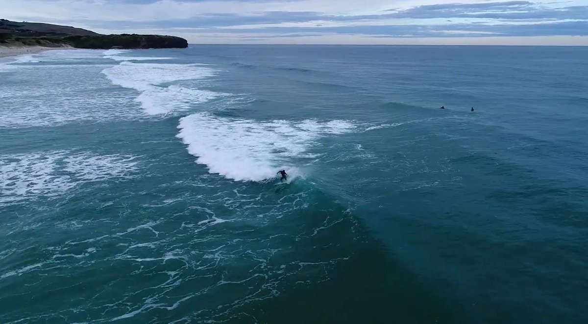A surfer drops in toward the headland end of the beach, peaks shifting along the sand, St Clair surf spot, Dunedin / Otago, N