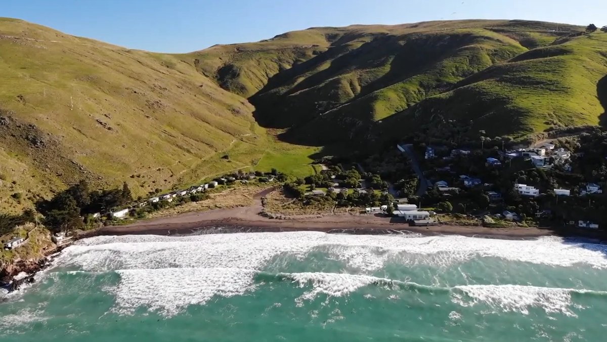The bay from above, lines of whitewater pushing onto the sand below the steep Banks Peninsula hills, Taylors Mistake surf spo