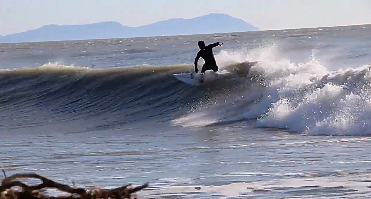 Driving off the bottom on a clean wall, the hills across the water hazy on the horizon, The Cut (Blenheim) surf spot, Marlbor