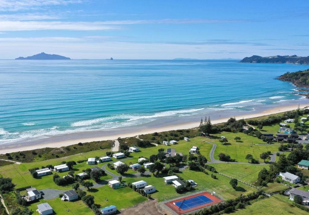 Camp Waipu Cove tucked behind the dunes with Bream Bay opening up, Waipū Cove surf spot, Northland East, New Zealand.