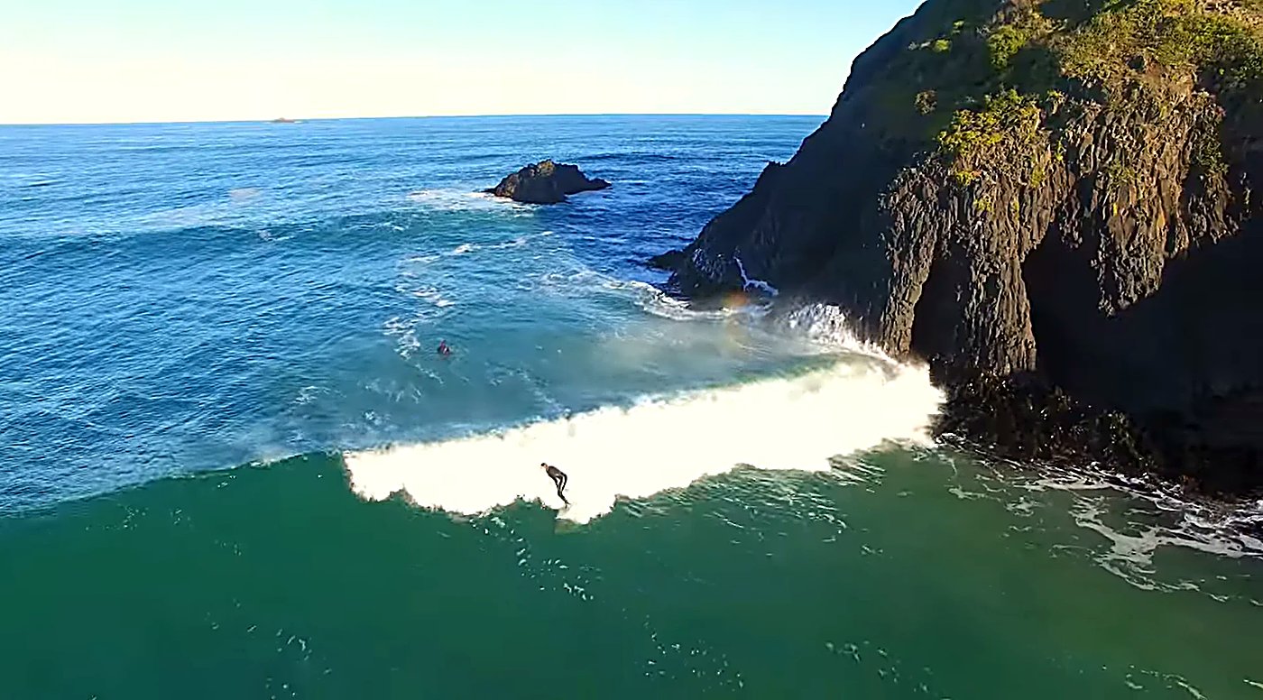 A lone surfer threads the wave around the basalt sea stack on a sunny day at Whareakeake, Whareakeake / Murdering Bay surf sp